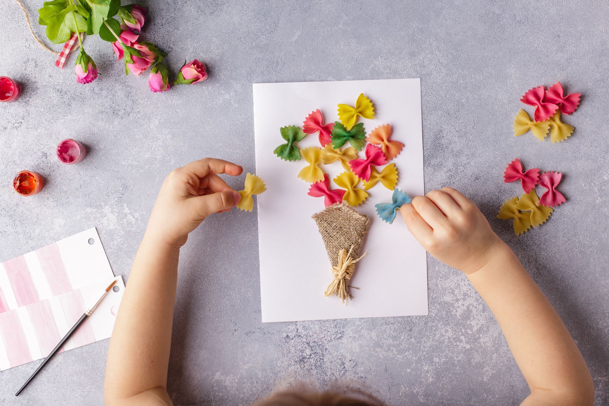 Paper crafts for mother day, 8 march or birthday. Small child doing a bouquet of flowers out of colored paper and colored pasta