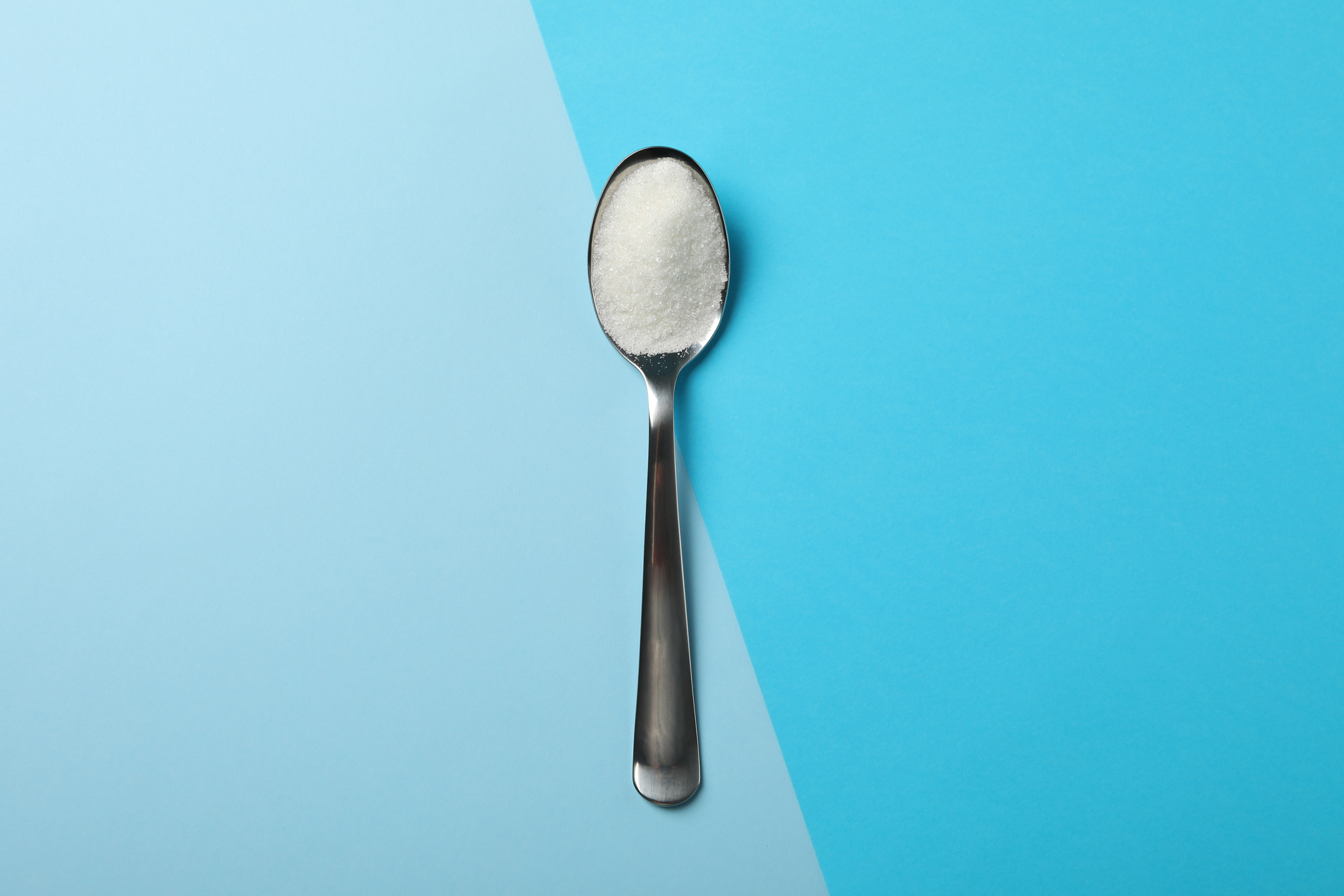 Spoon with sugar on two tone background, space for text