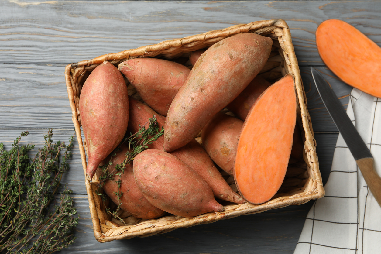 Sweet potato in basket on wooden background, top view