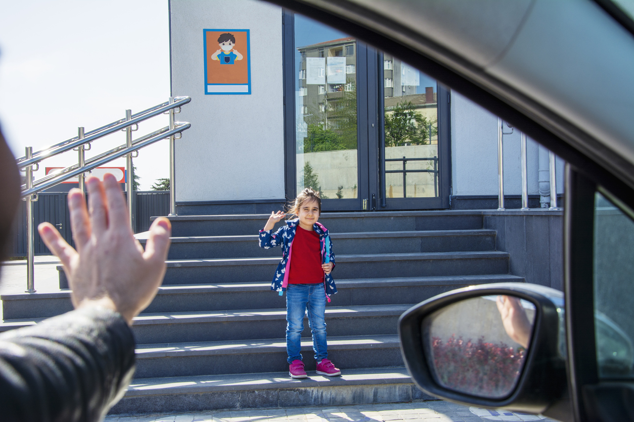 Little girl waving and winking at her father as her dad dropped him off at school