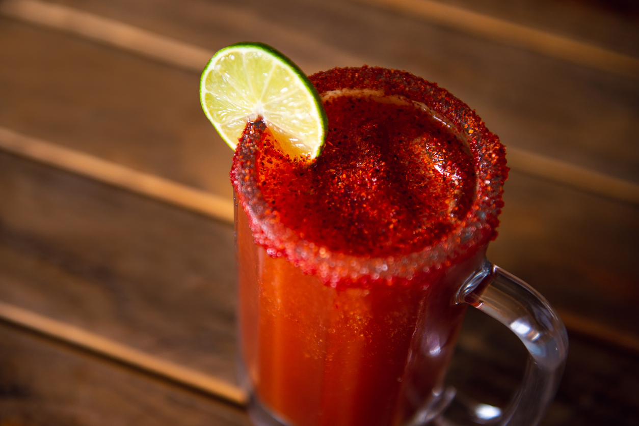 Michelada beer with tomato juice. Clamato with beer on wooden table.