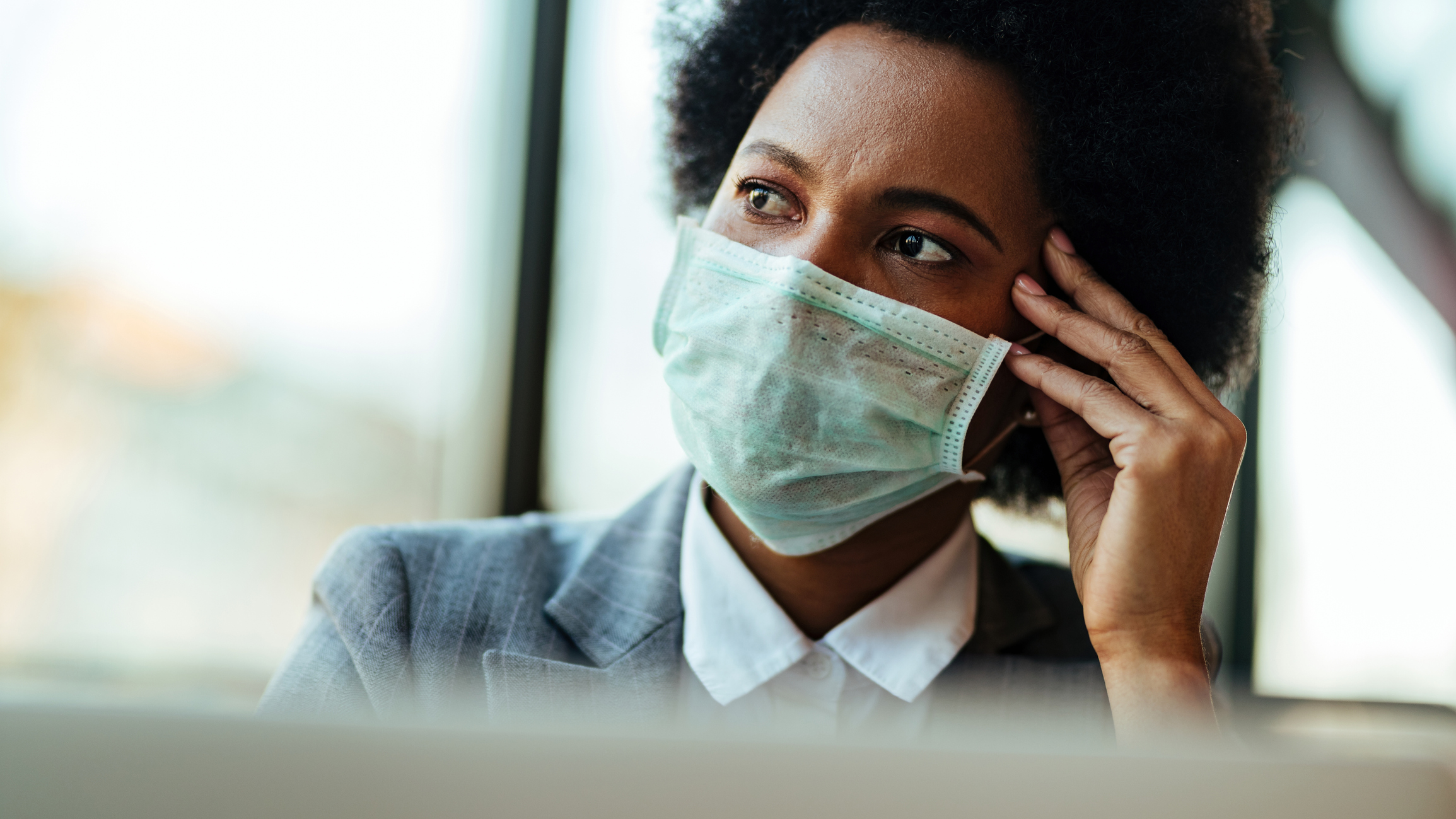 Worried African American businesswoman with protective mask thinking of something in the office.