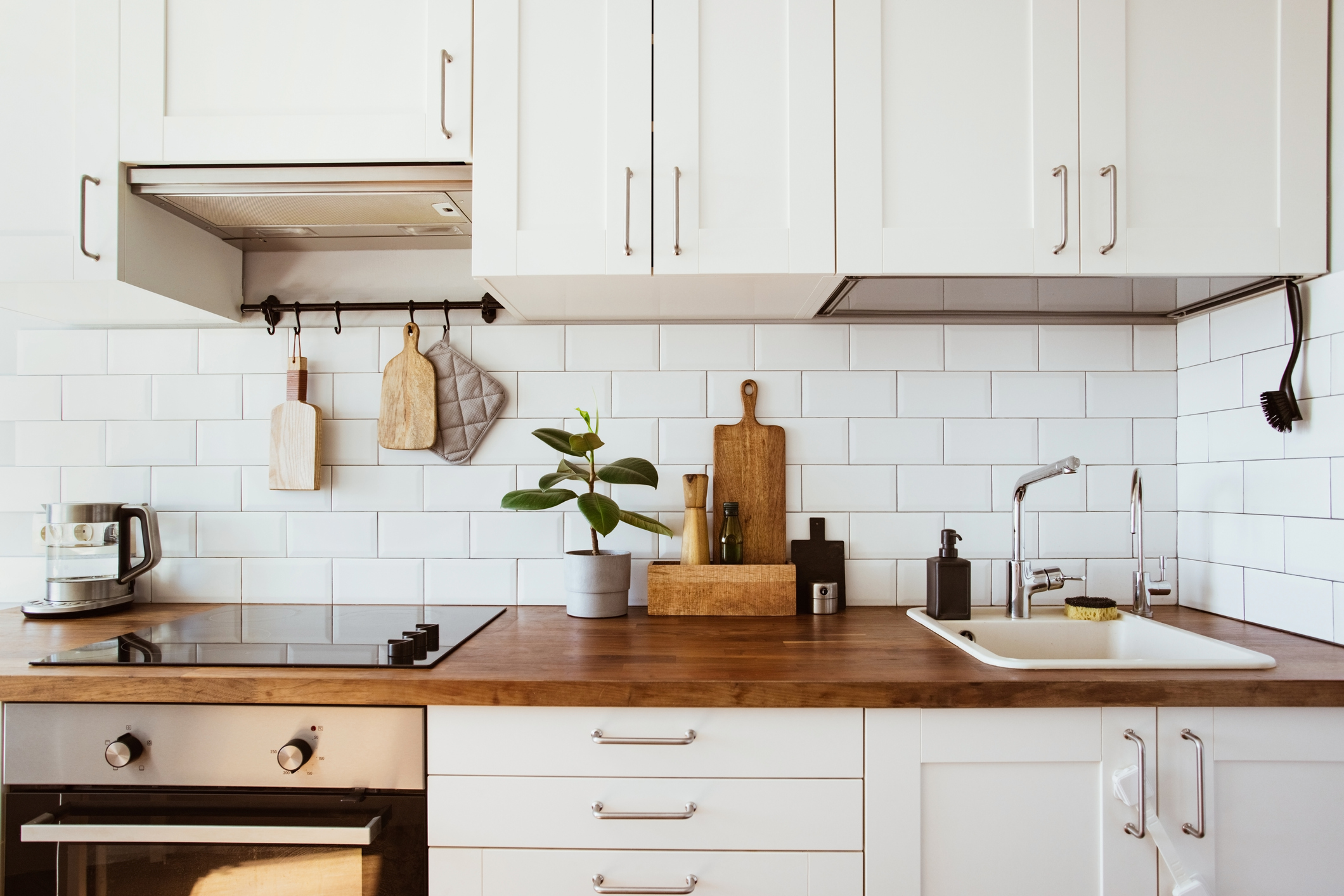 Kitchen brass utensils, chef accessories. Hanging kitchen with white tiles wall and wood tabletop.Green plant on kitchen background