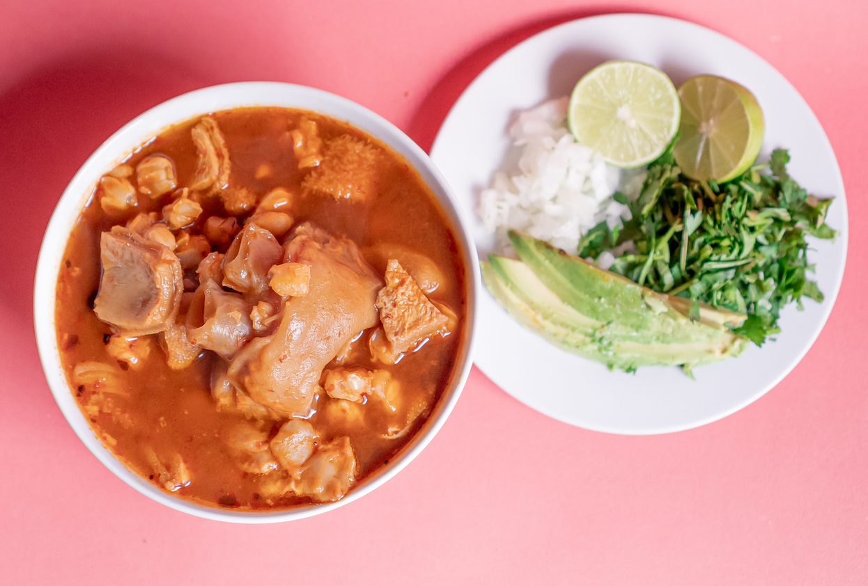 Delicious Mexican Menudo on a white plate accompanied by a dish with condiments on the side.