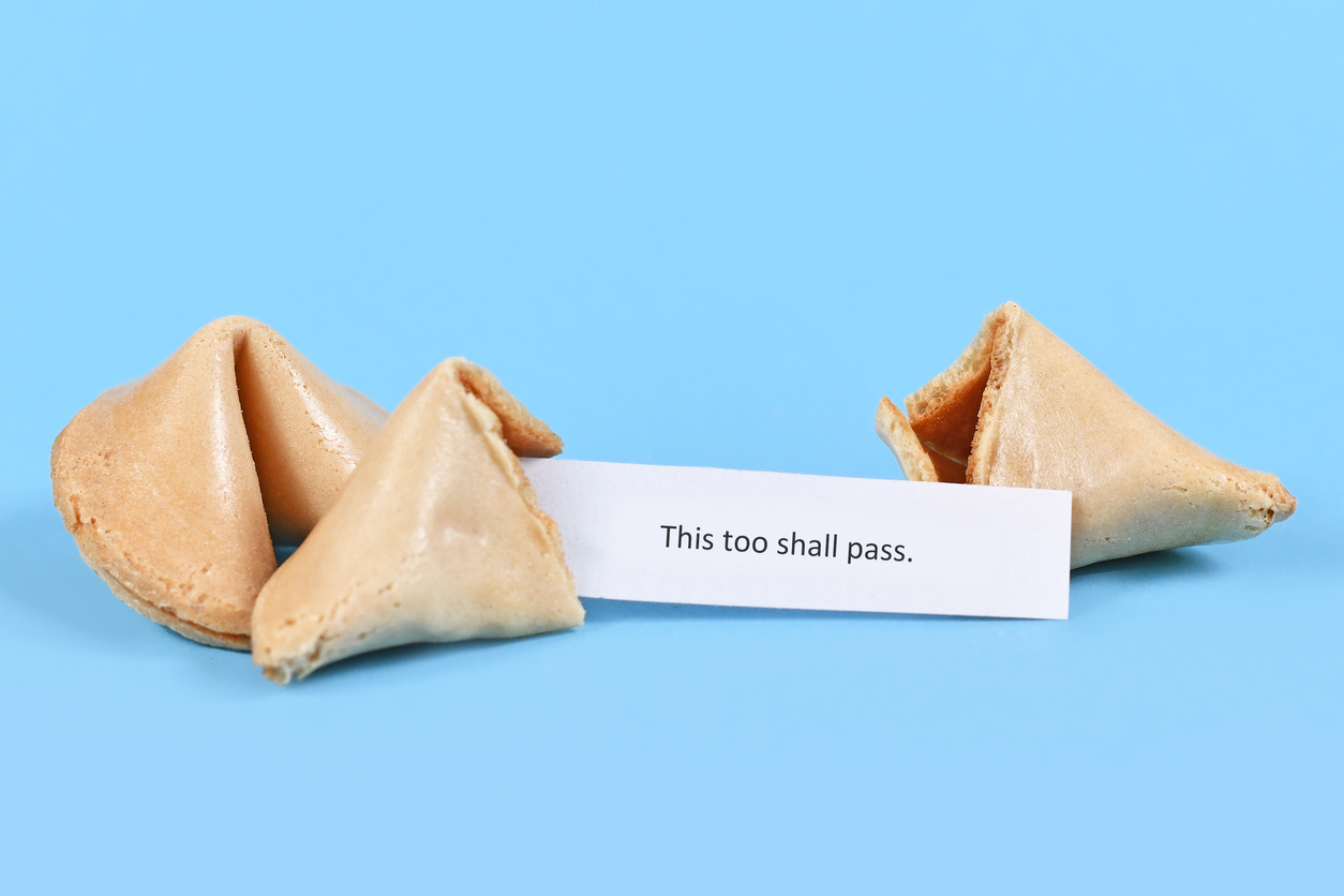 Broken up and whole fortune cookie with motivational text 'This too shall pass' on paper note on blue background