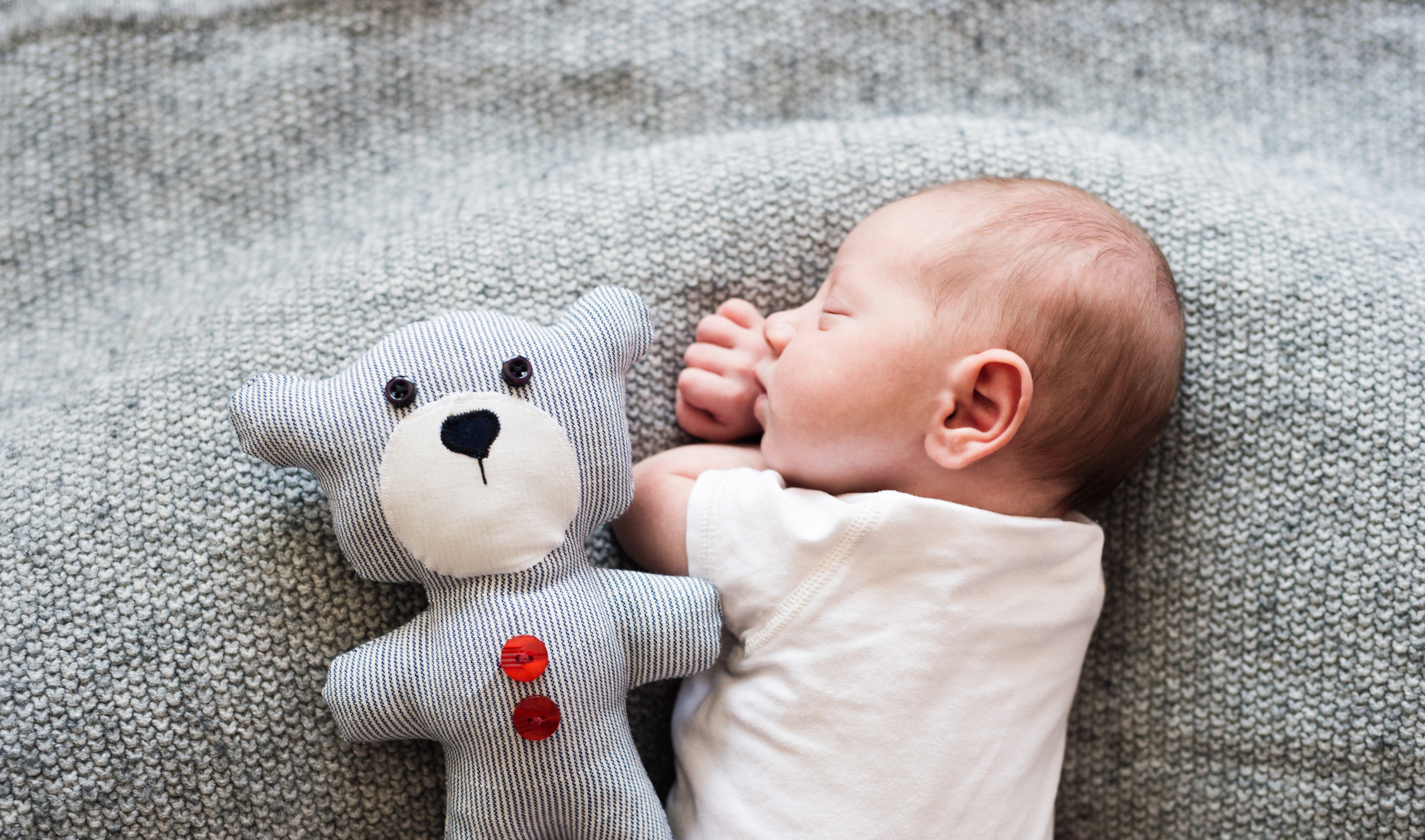 Newborn baby boy lying on bed with teddy bear, sleeping