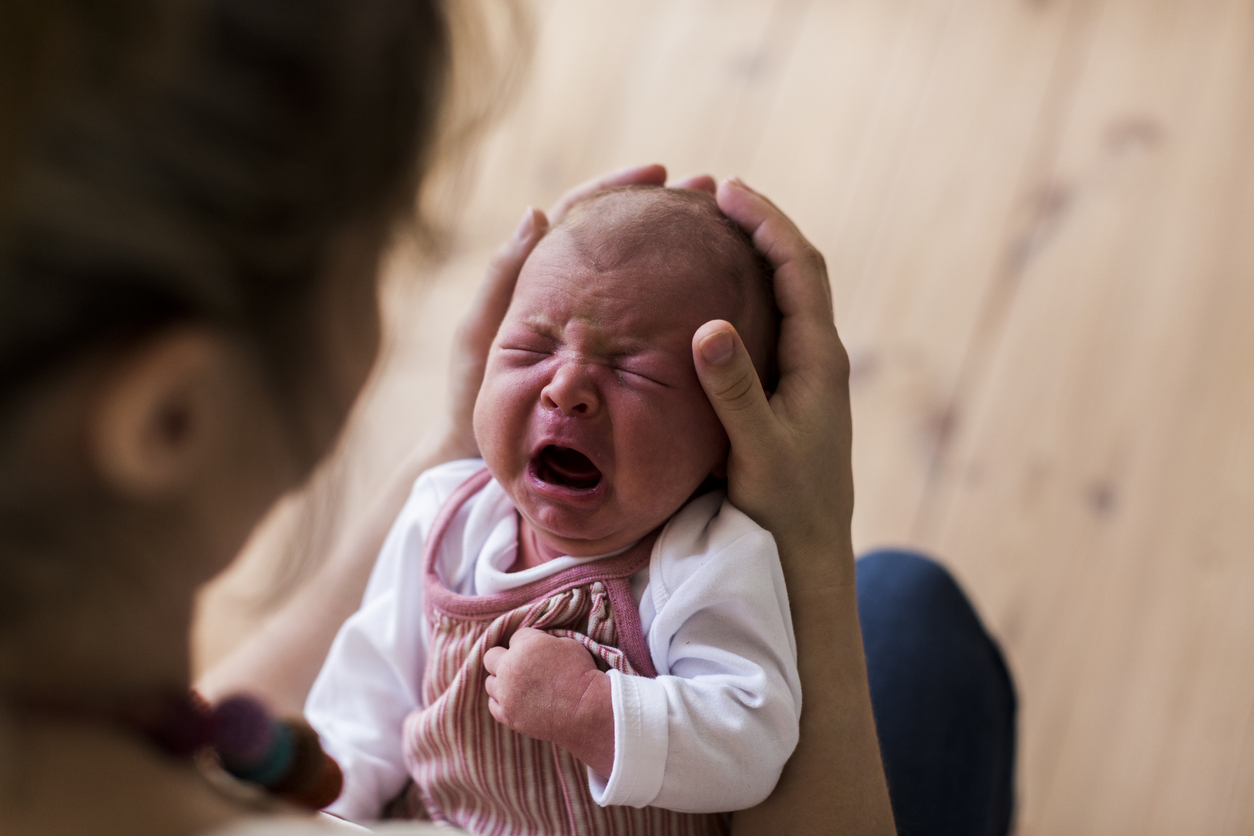 Unrecognizable mother holding crying newborn baby girl.