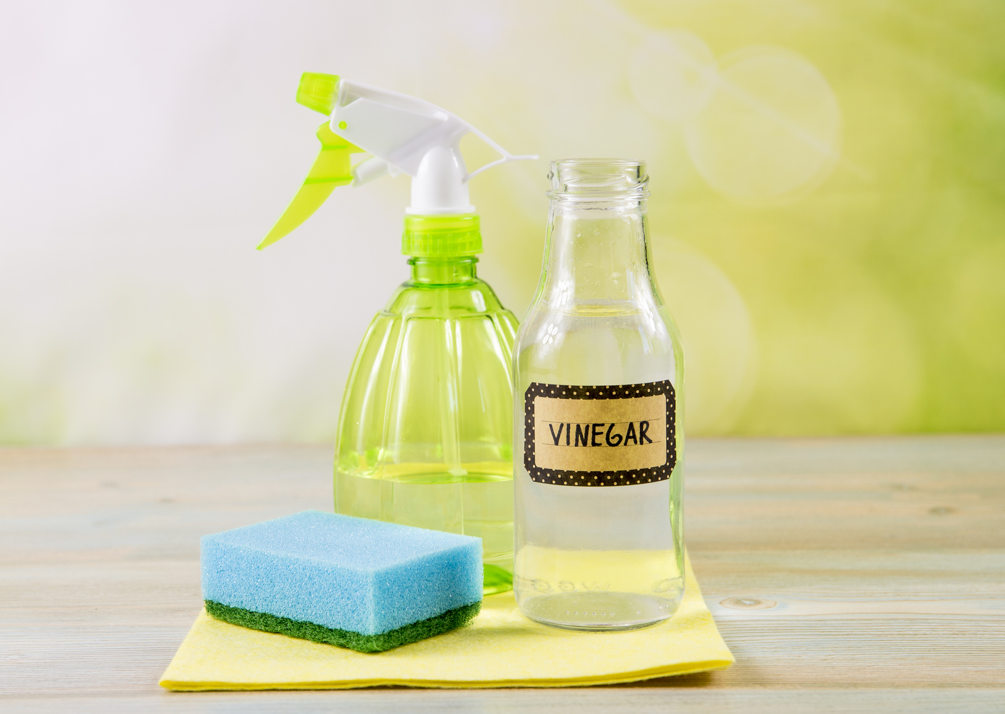 Chemical free home cleaner products concept. Using natural destilled white vinegar in spray bottle to remove stains. Tools on wooden table, green bokeh background, copy space.