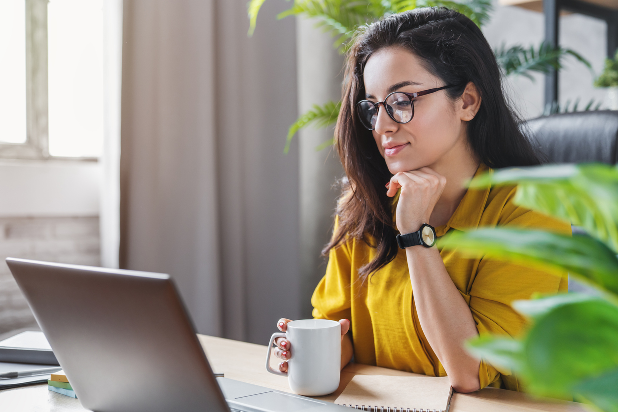 Young woman enjoying her coffee while working or studying on laptop computer at home office