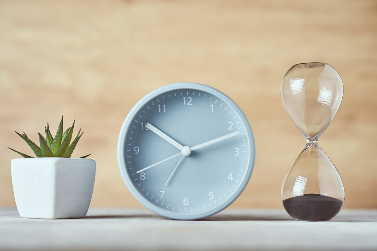 Hourglass, alarm clock and plant on the table, close up