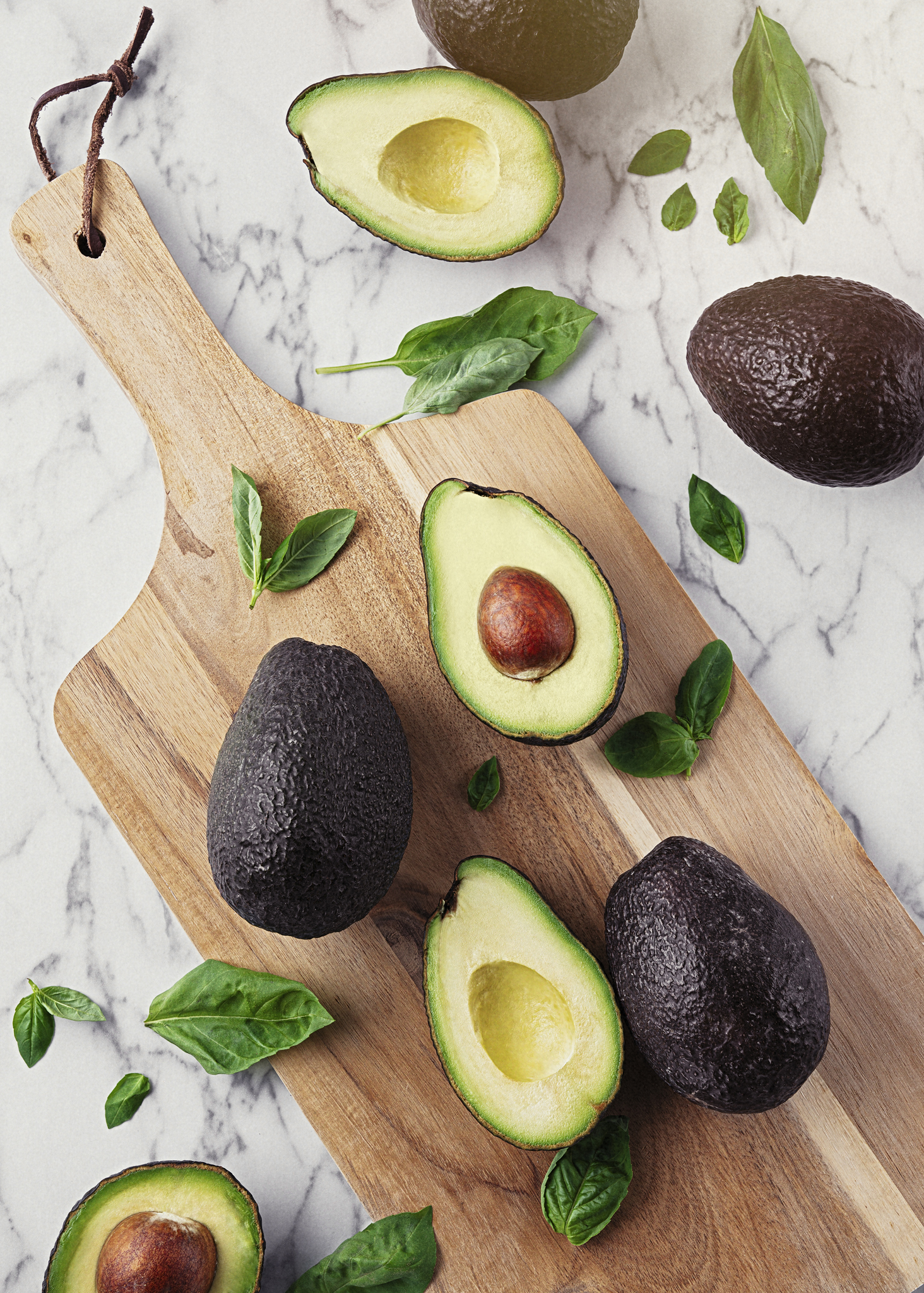 Wooden table with avocados and basil on marble stone