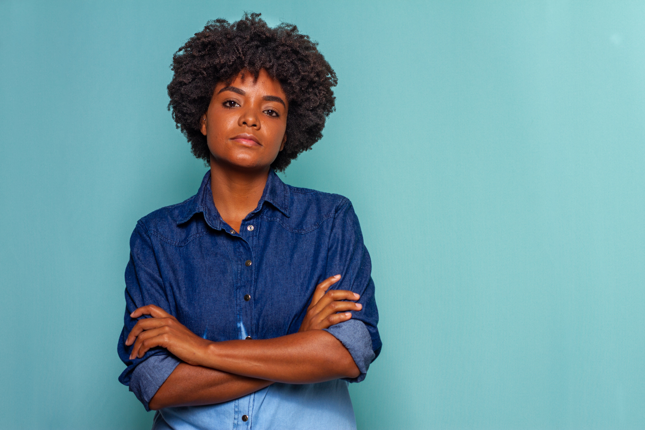 Black young woman with black power hair wearing a blue jeans shirt on blue background