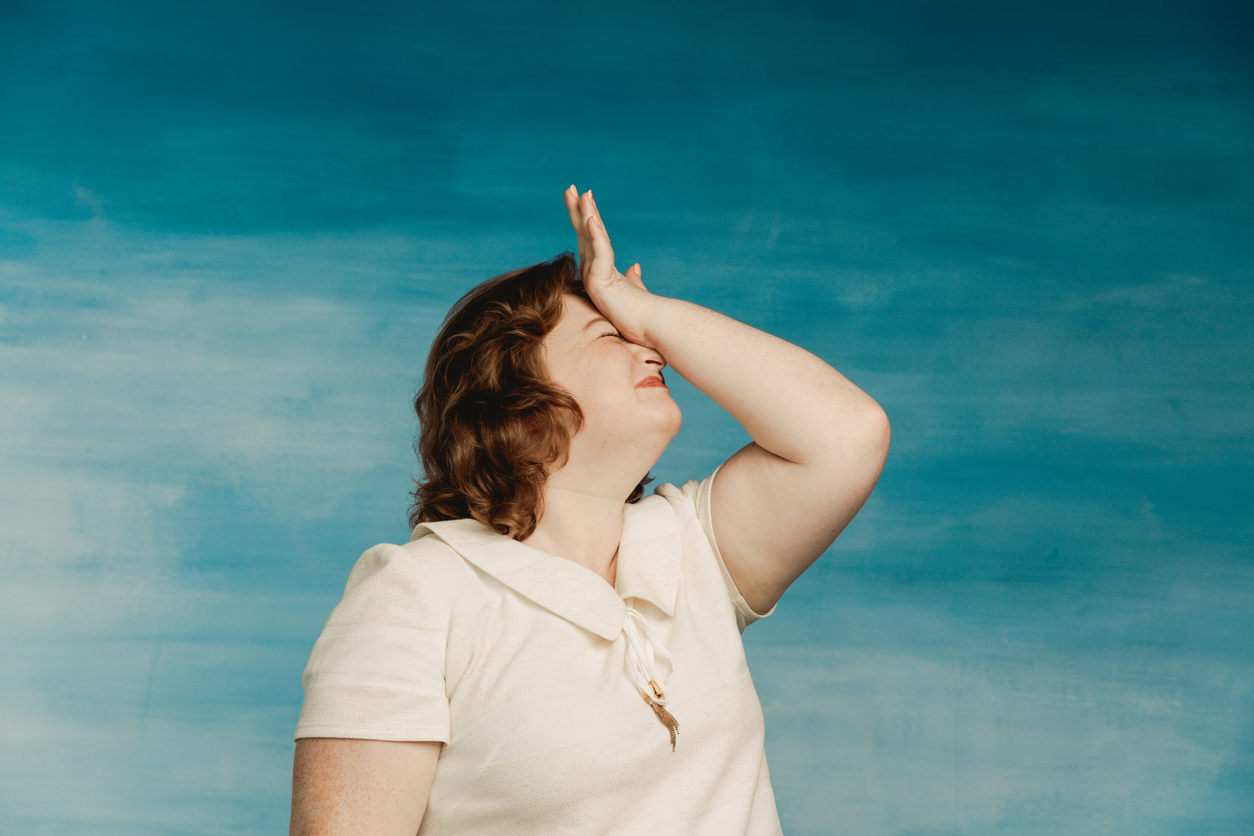 Funny plump woman in a white dress demonstratively suffers by hitting himself on the forehead on a blue background.