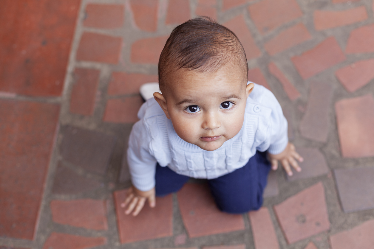 Baby kneeling on the floor looking up in a portrait