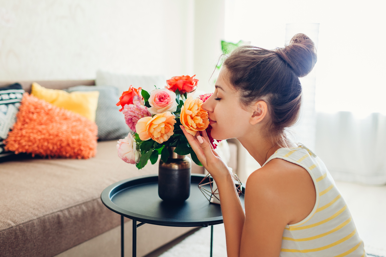 Woman smelling fresh roses in vase on table. Housewife taking care of coziness in apartment. Interior and decor