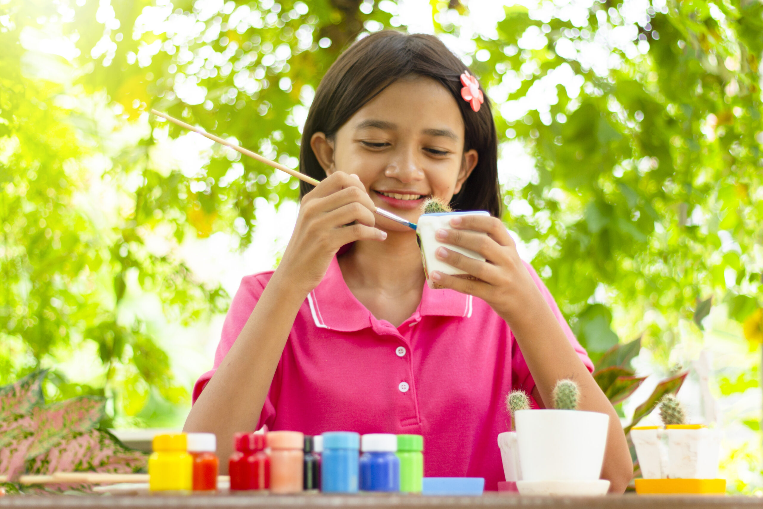 Happy Asian young girl painting color on cactus pot with green nature background.