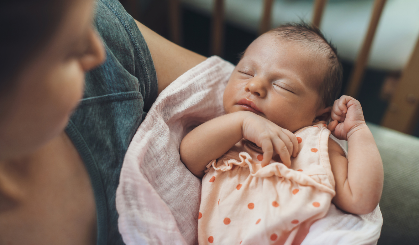 Newborn baby sleeping in safety while mother is holding and smiling at her