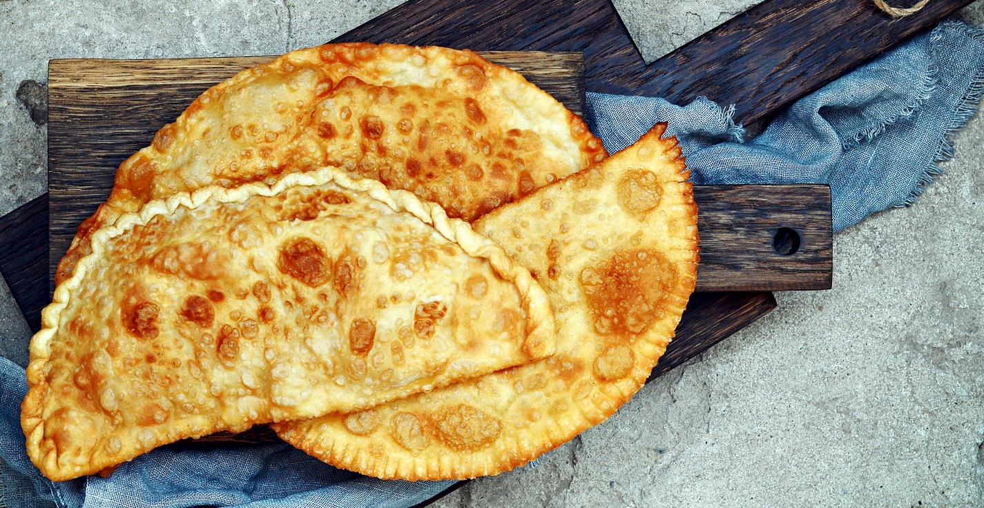 Uzbek eastern Tatar cuisine, cheburek with meat and suluguni cheese and greens on a wooden board. Cheburek - fried pie with meat and onions. Traditional dish of Turkish and mongolian,pasties empanada