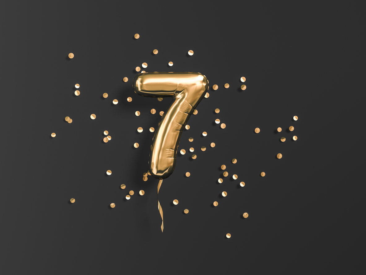 Number 7 flying foil balloon and gold confetti on black. Seven-year anniversary background