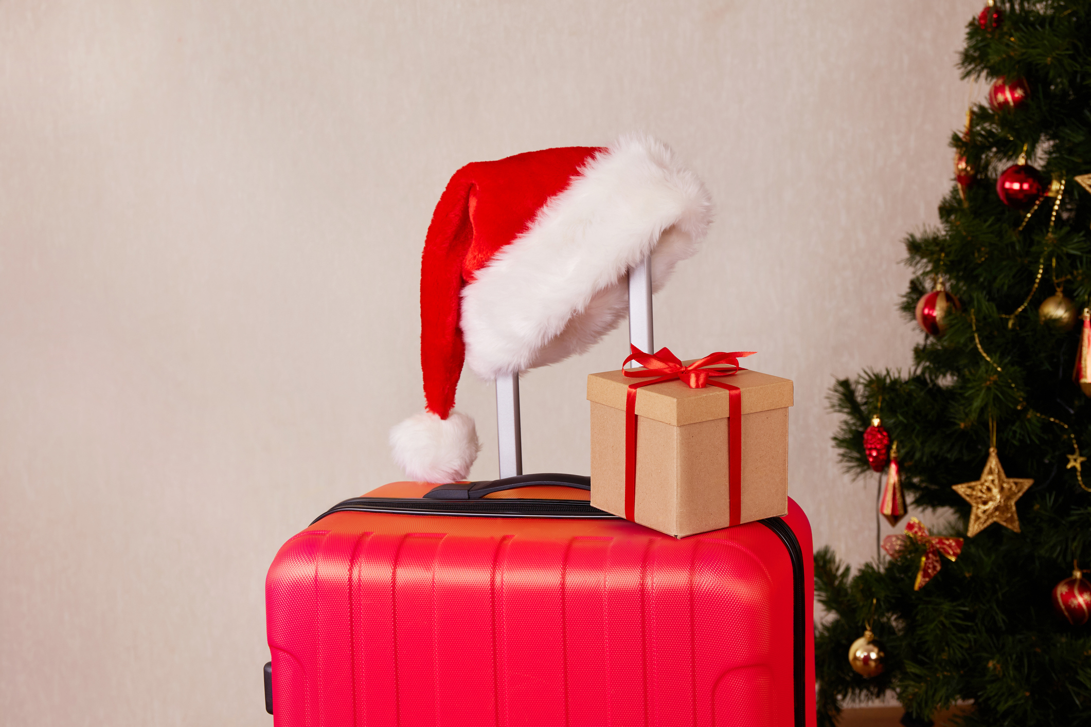 A red suitcase, a Santa Claus hat and a gift box. The concept of traveling for Christmas.