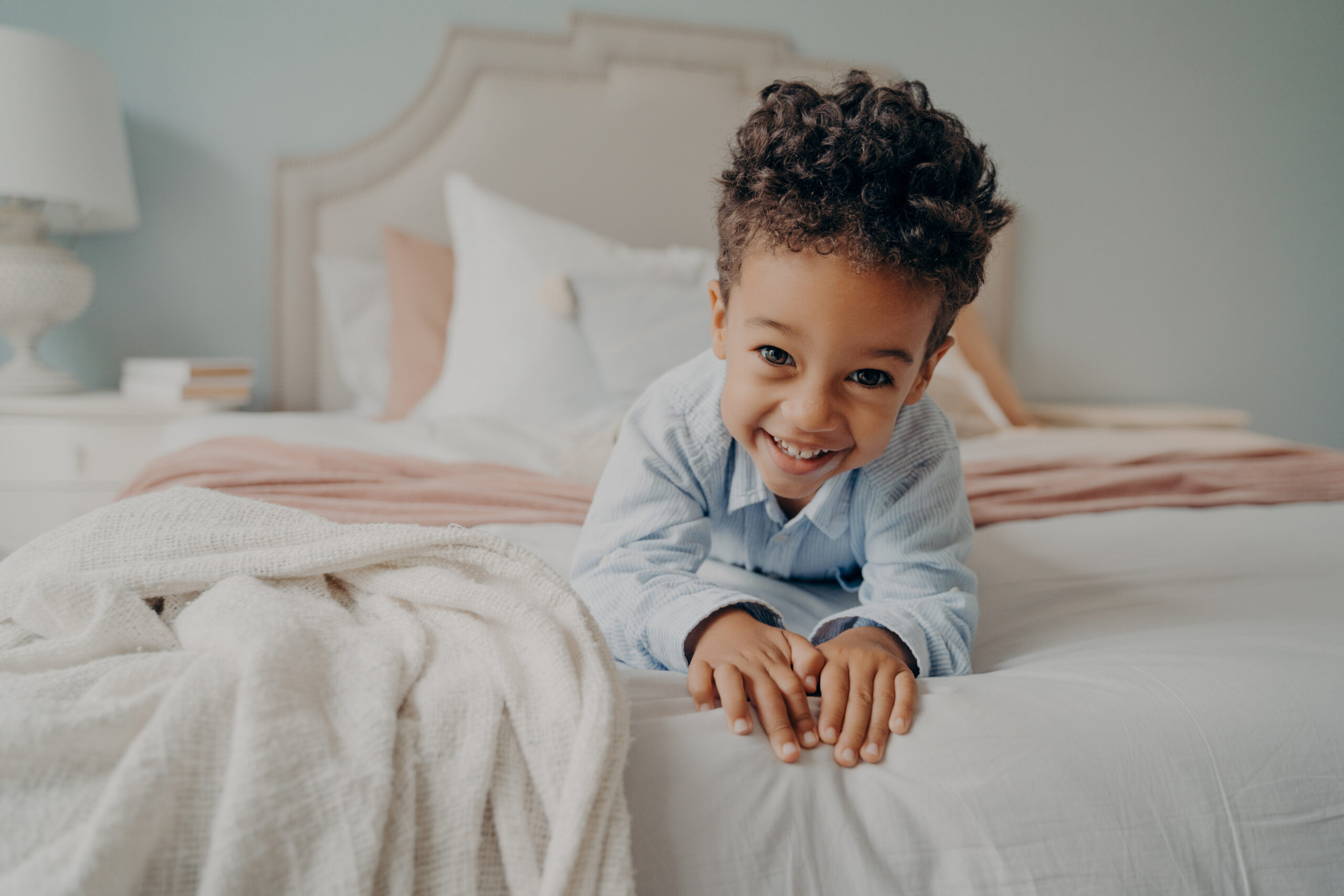 Happy curly afro american boy laying on bed and smiling at camera