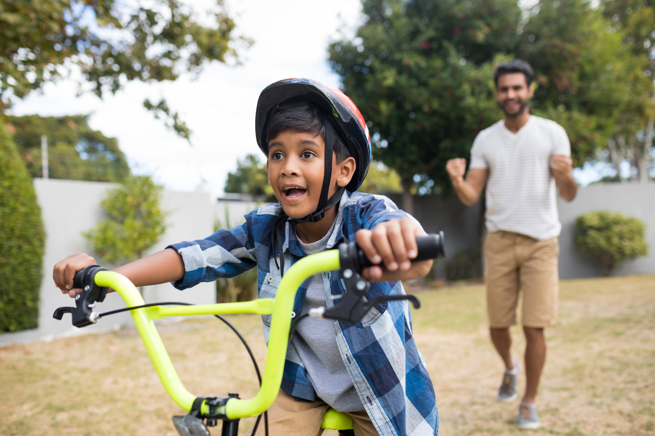 Boy cycling with father standing in background