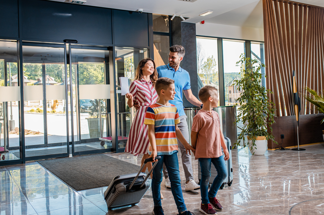 Smiling family of four enters to the hotel lobby to check in at the reception for vacation.