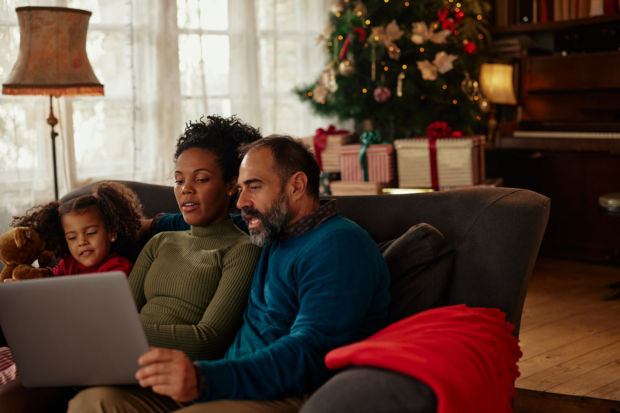 Diverse parents and daughter using tablet on sofa at home