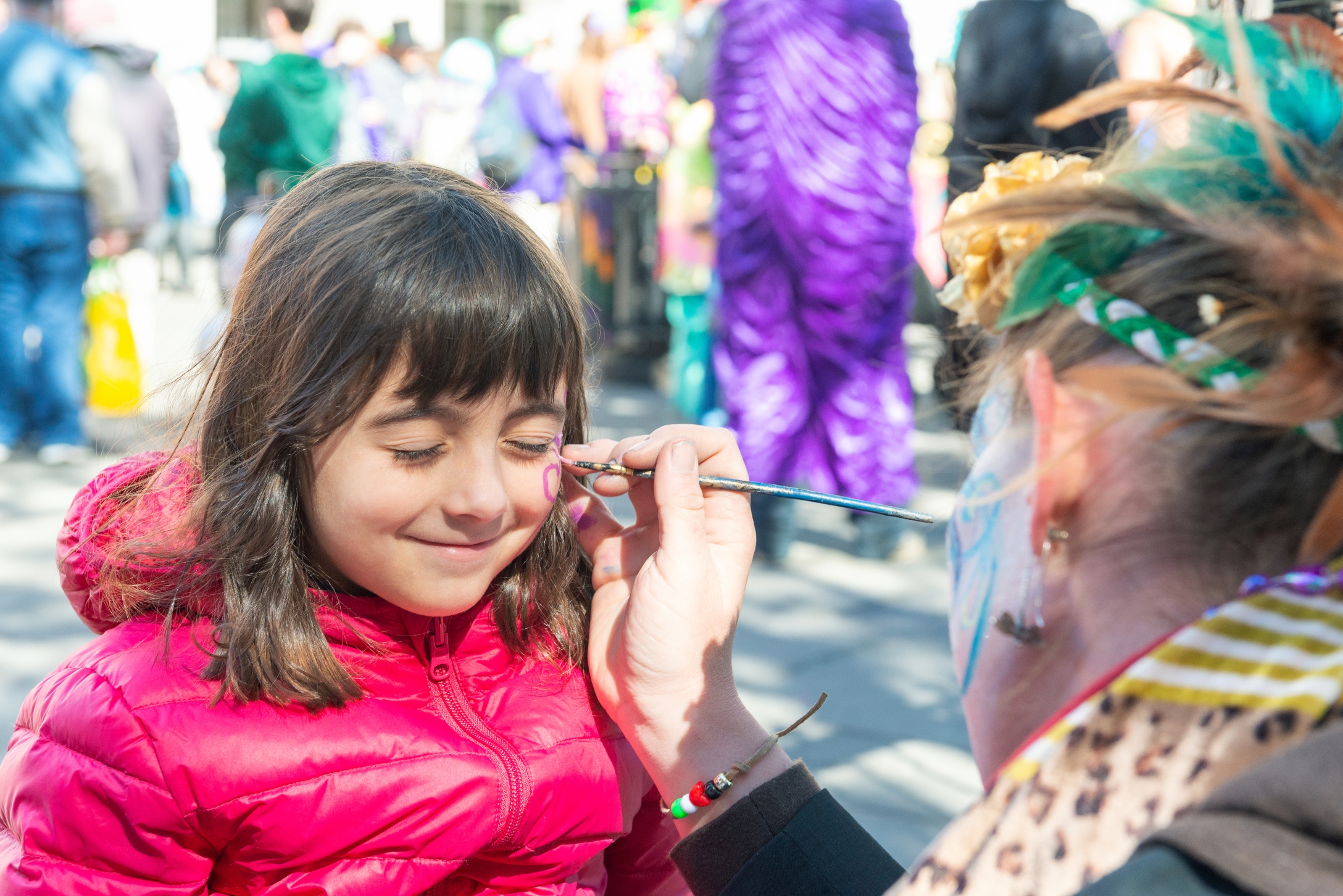 Smiling little girl getting her face painted by the face painter artist.