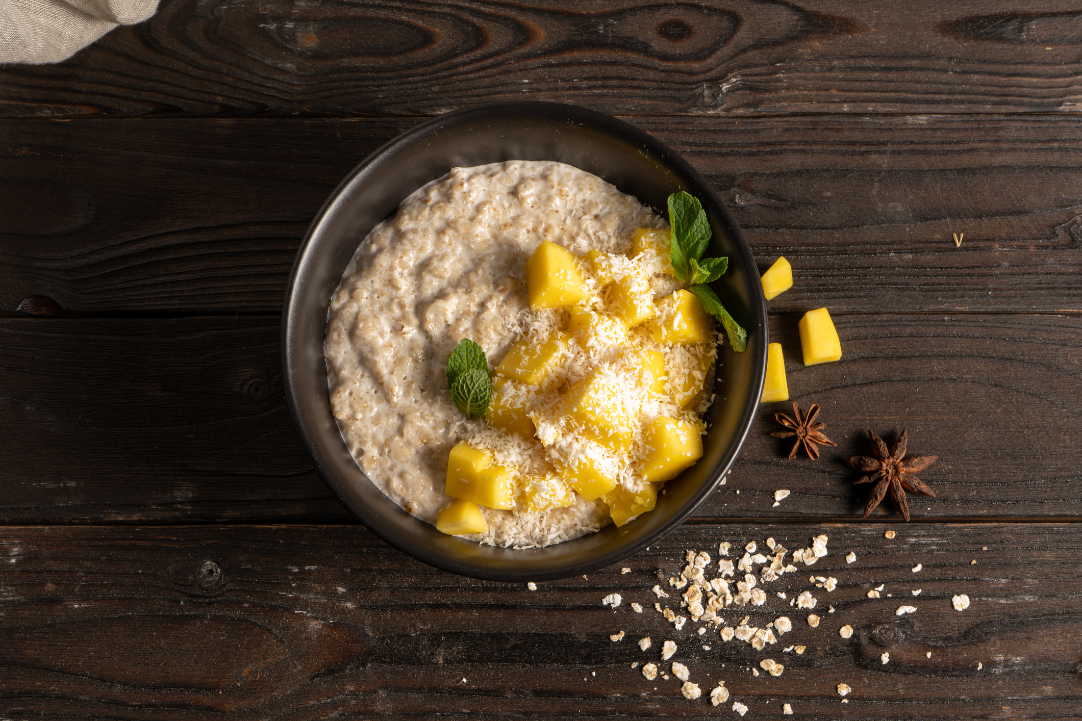 Hot oatmeal with fresh mango pieces, cooked in milk and garnished with mint chanterelles. Healthy diet vegetarian breakfast in a round ceramic bowl on a wooden kitchen table.