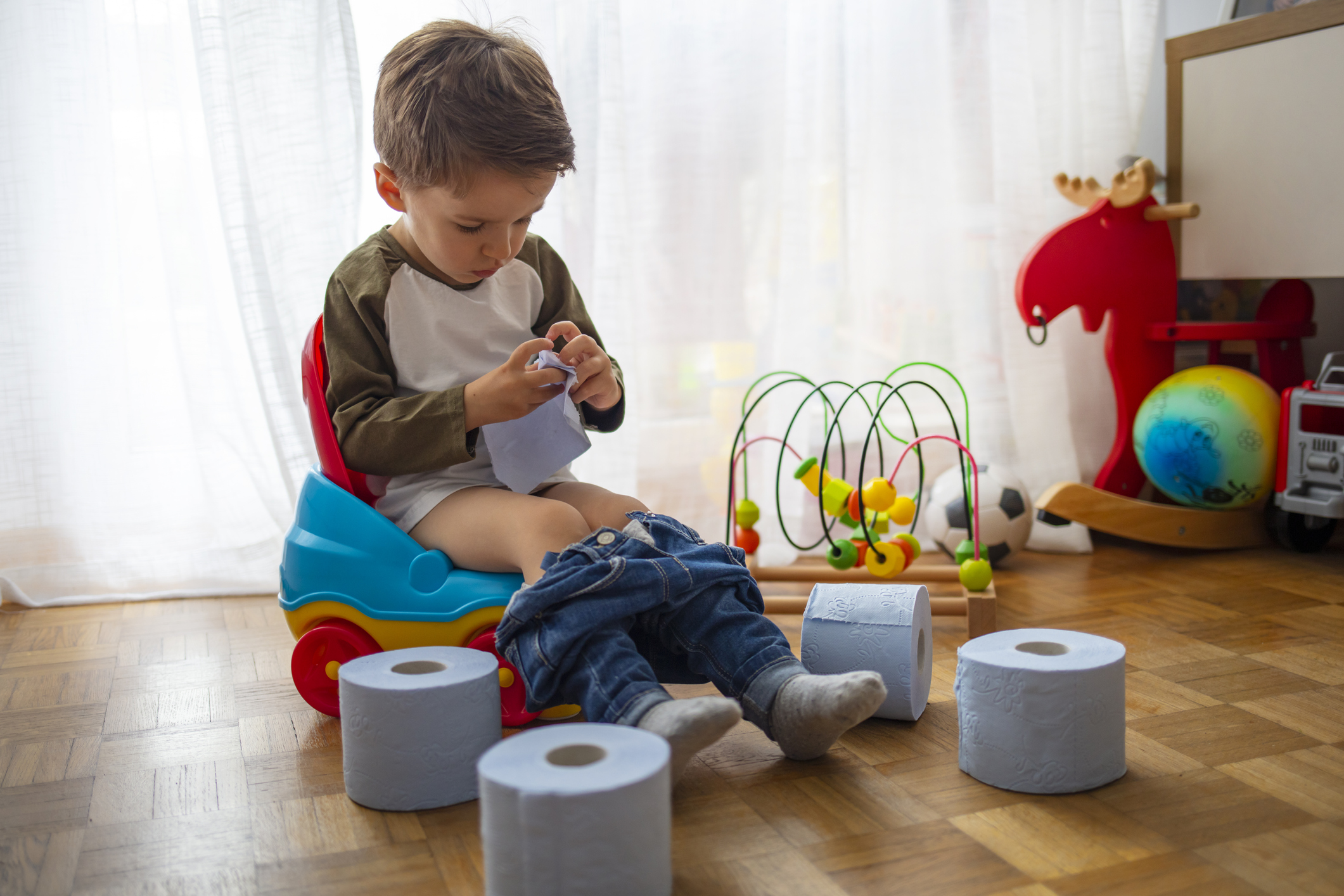 Little toddler boy, sitting on potty, playing with toilet paper.