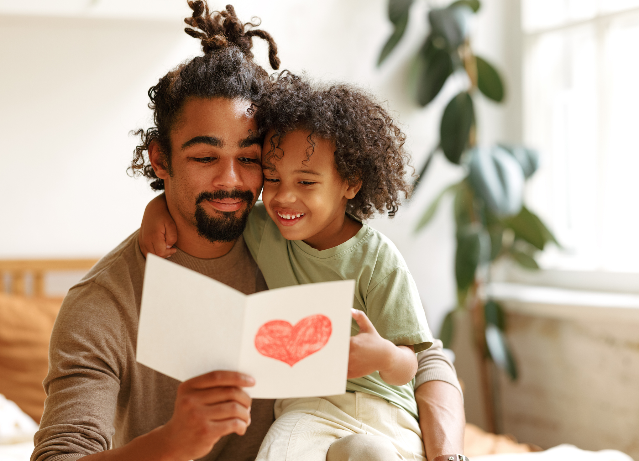 Cute african american little boy son giving his father handmade greeting postcard on Fathers Day