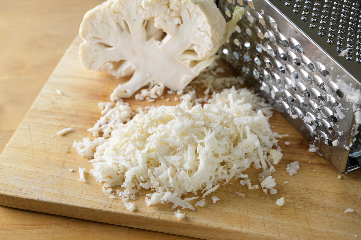 Grating cauliflower with a metal grater on a wooden kitchen board, used as rice replacement for a healthy low carb or ketogenic diet meal