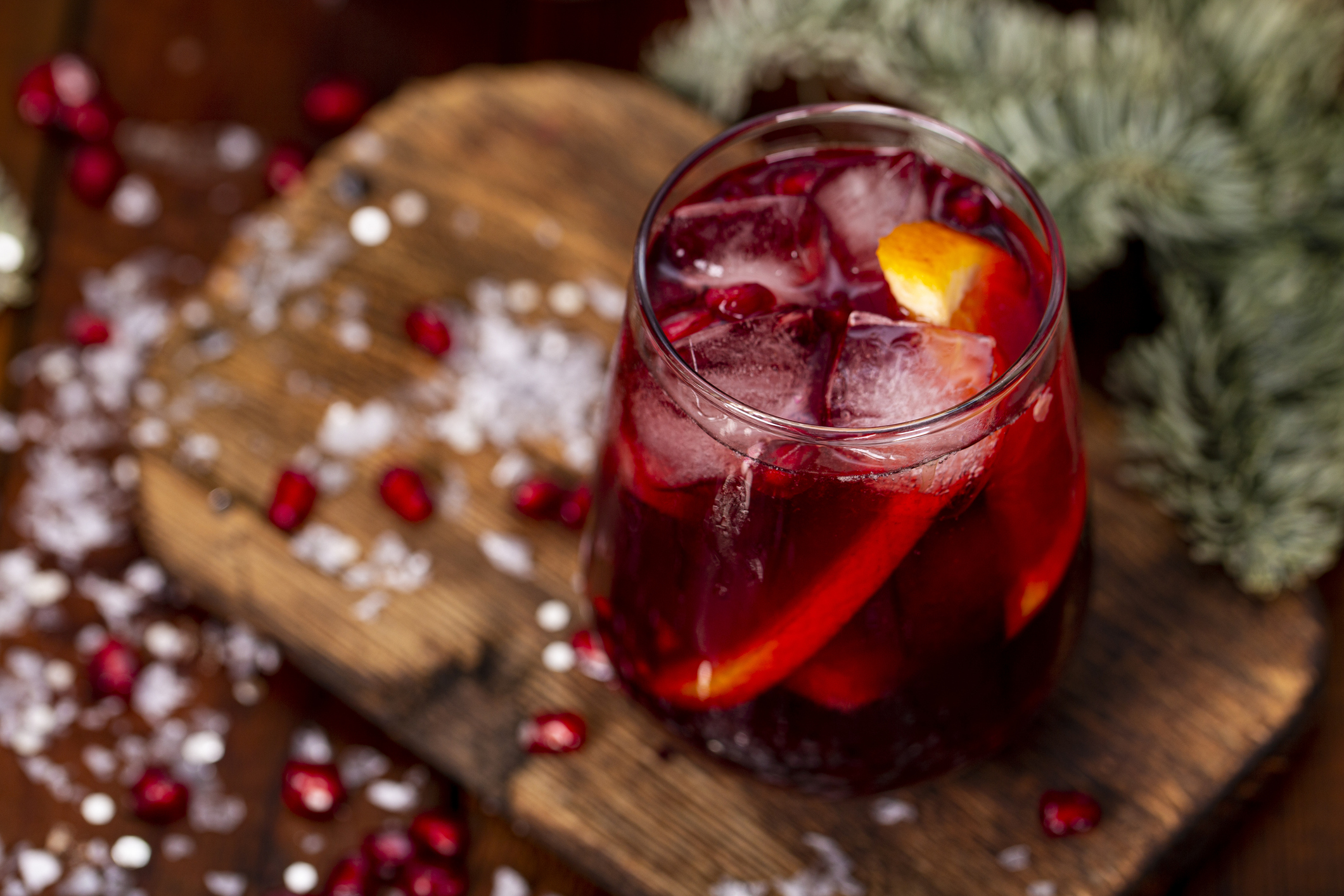 A glass of pomegranate cocktail with orange on the background of Christmas decorations and lights. Festive winter drink