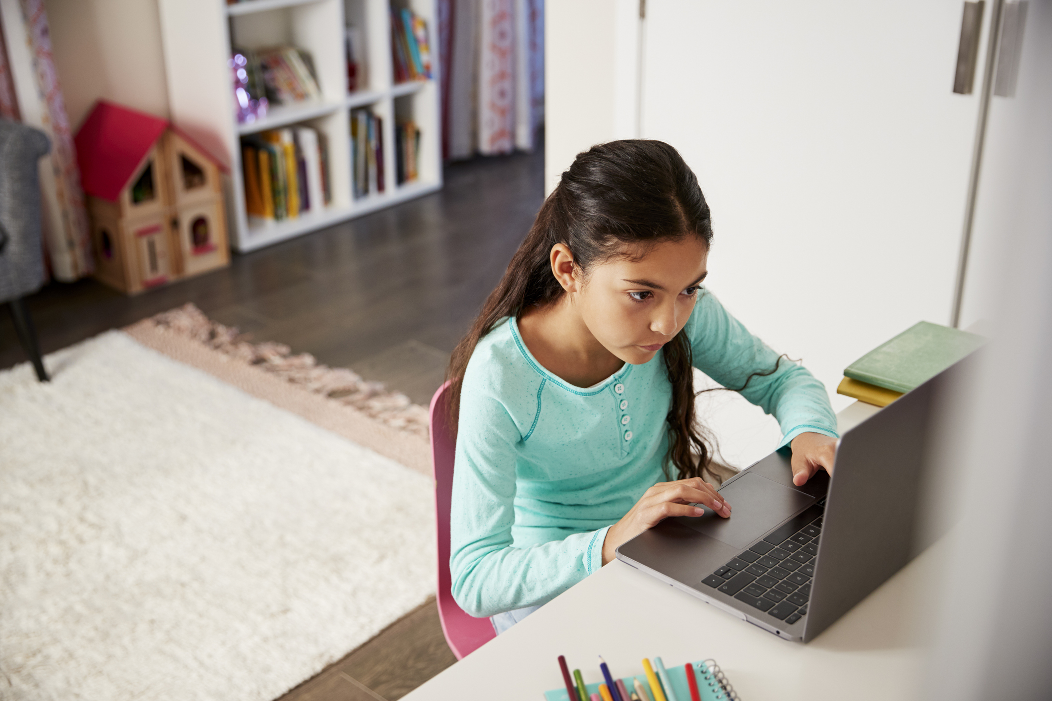 Young Girl Sitting At Desk In Bedroom Using Laptop To Do Homework