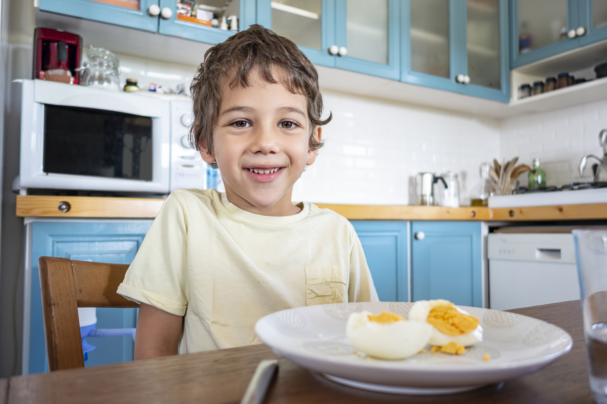 Small happy three year old boy eats an egg