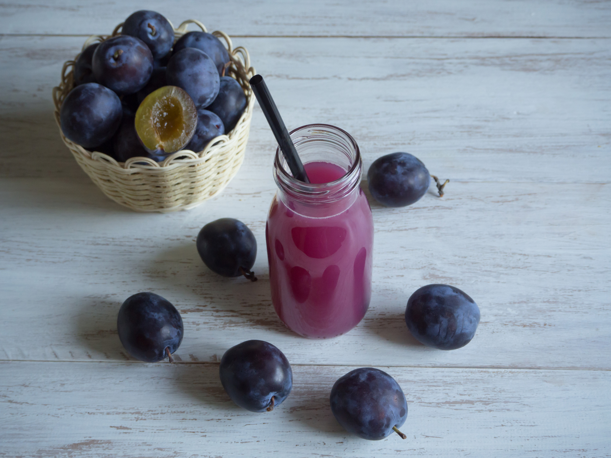 Plum juice and fresh plum on a white wooden table.