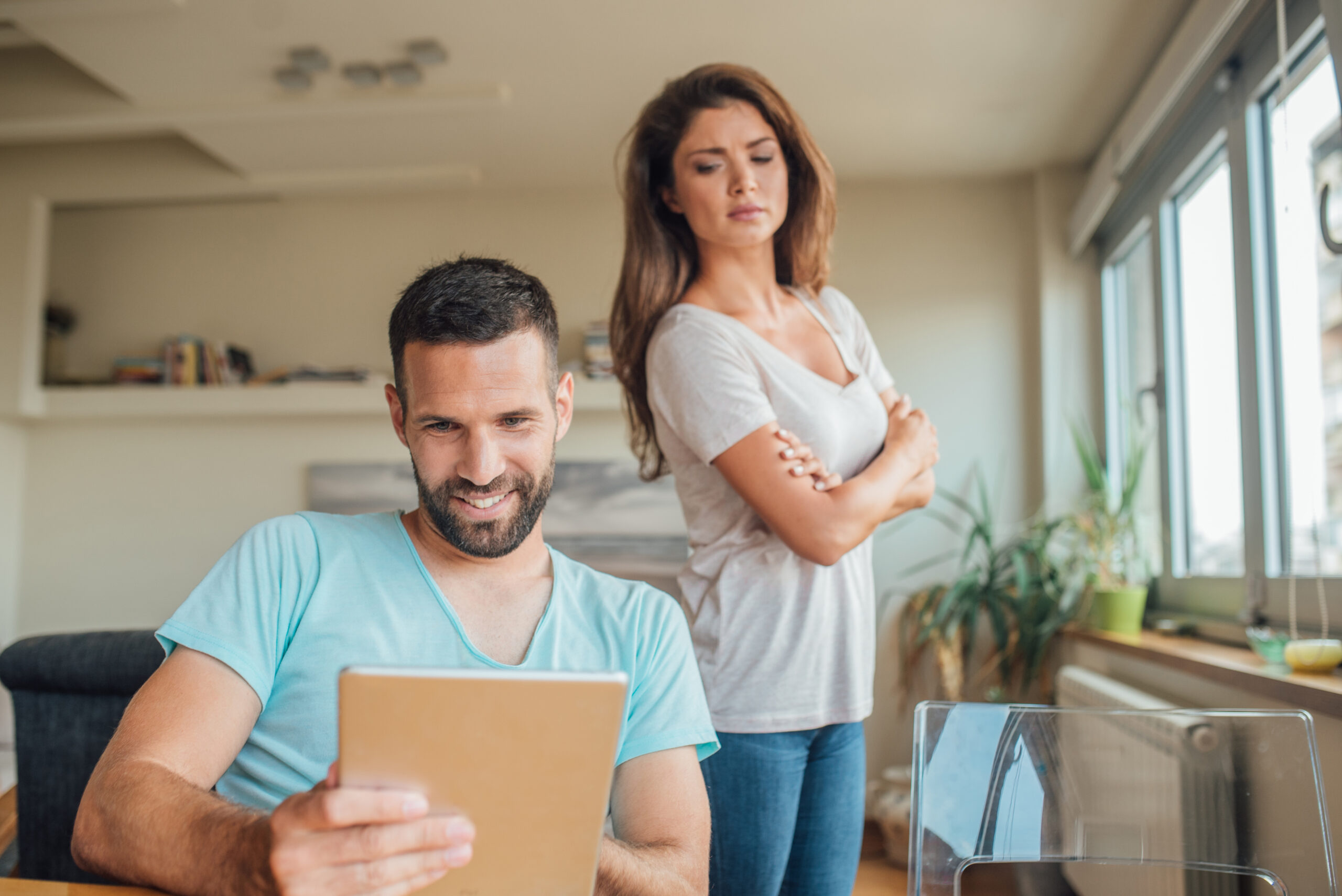 Young woman jealously looking at the smiling man using digital tablet