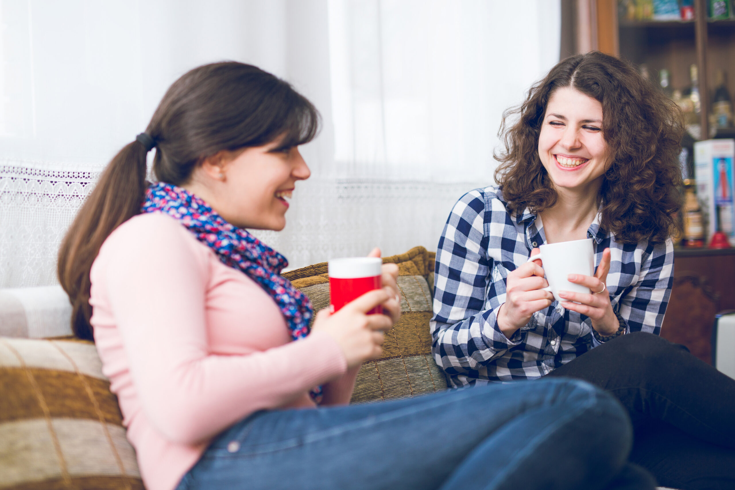 Two cheerful best girlfriends sitting on couch and talking.