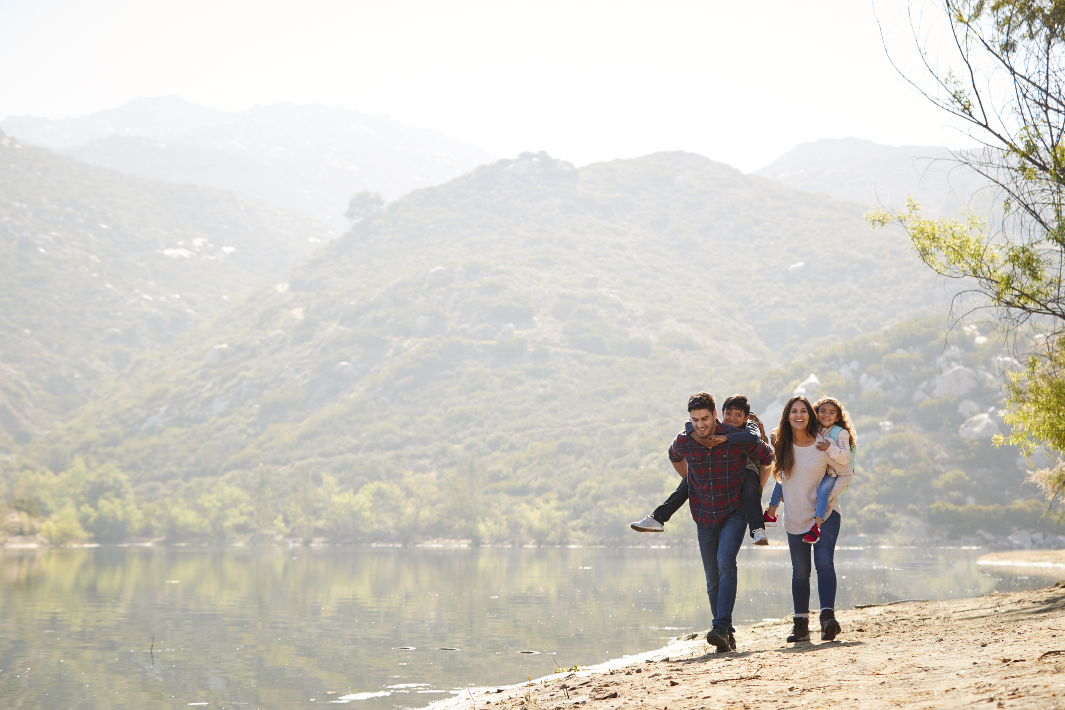 Parents piggybacking their young children by a mountain lake