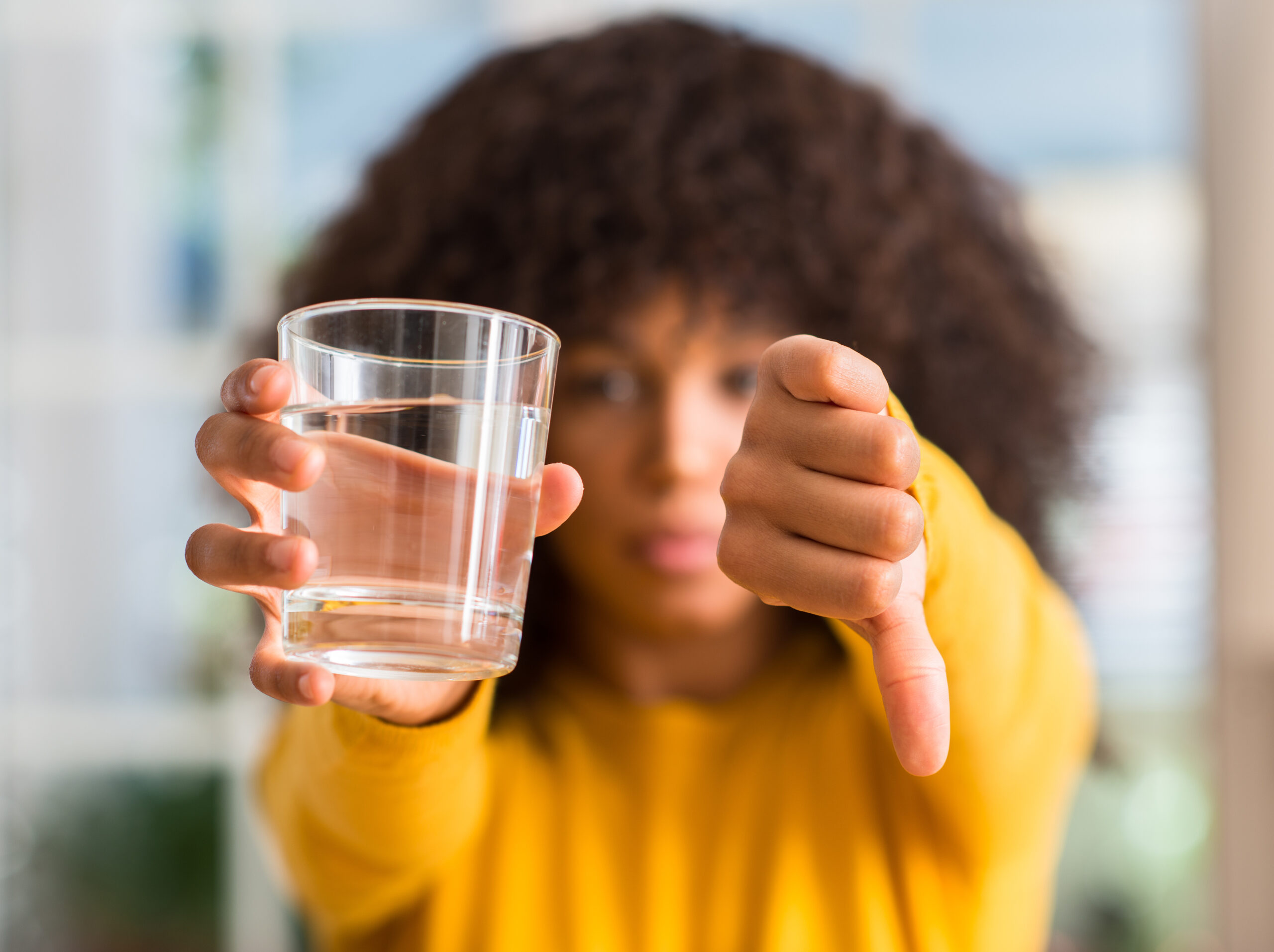 African american woman drinking a glass of water at home with angry face, negative sign showing dislike with thumbs down, rejection concept