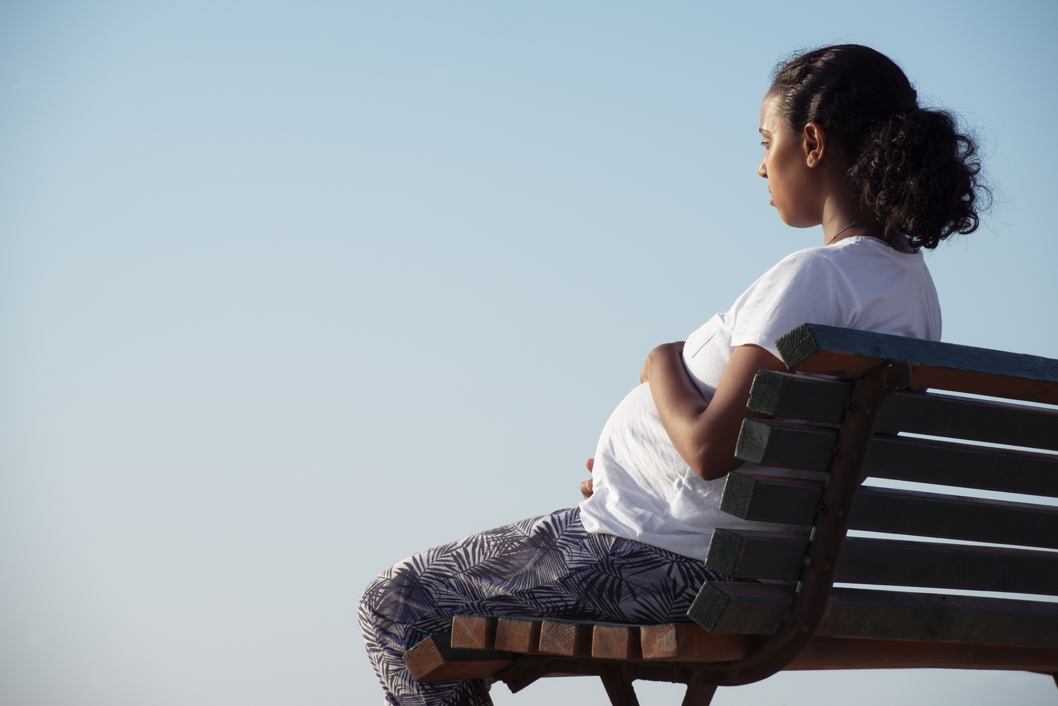 Relaxed pregnant woman sitting on a wooden bench.