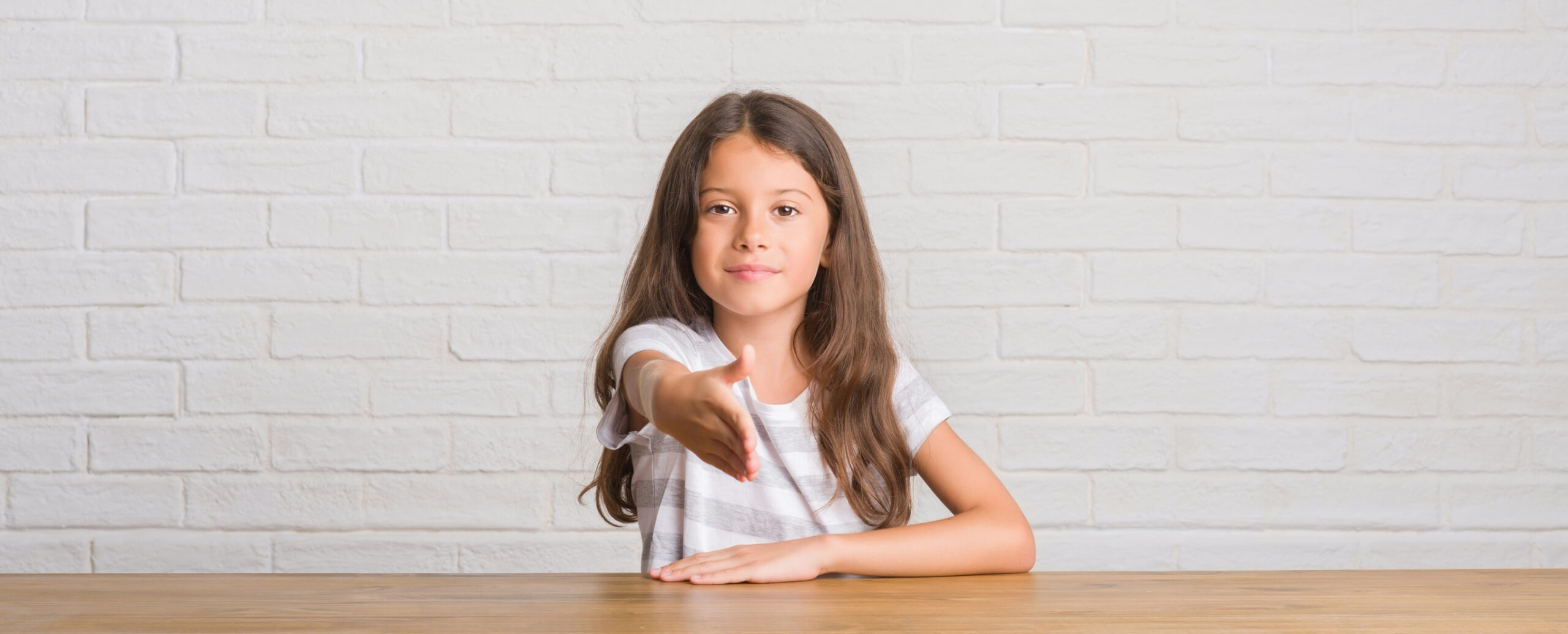 Young hispanic kid sitting on the table at home smiling friendly offering handshake as greeting and welcoming. Successful business.