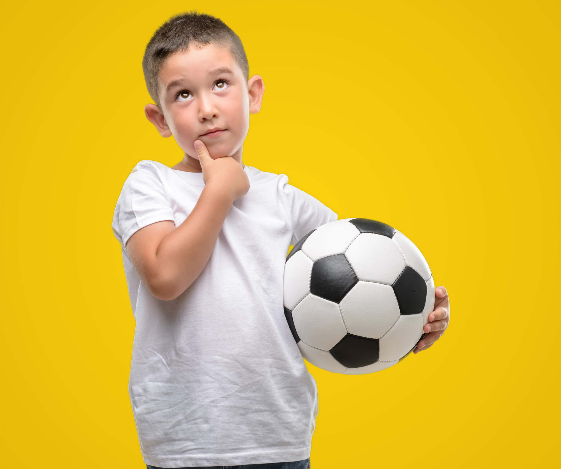 Dark haired little child playing with soccer ball serious face thinking about question, very confused idea