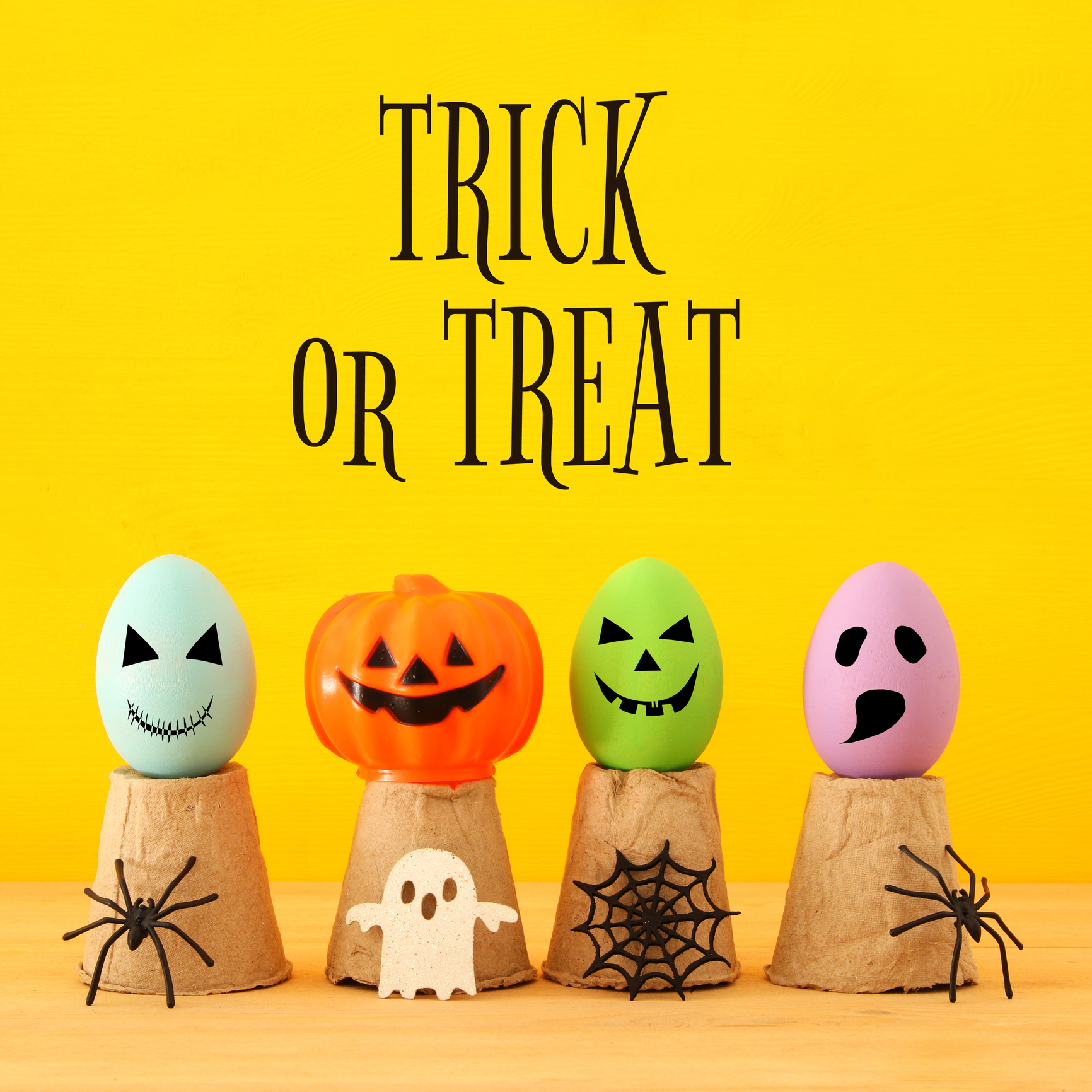 Halloween holiday concept. Colorful eggs with funny, scary and cute faces, spiders over wooden table.