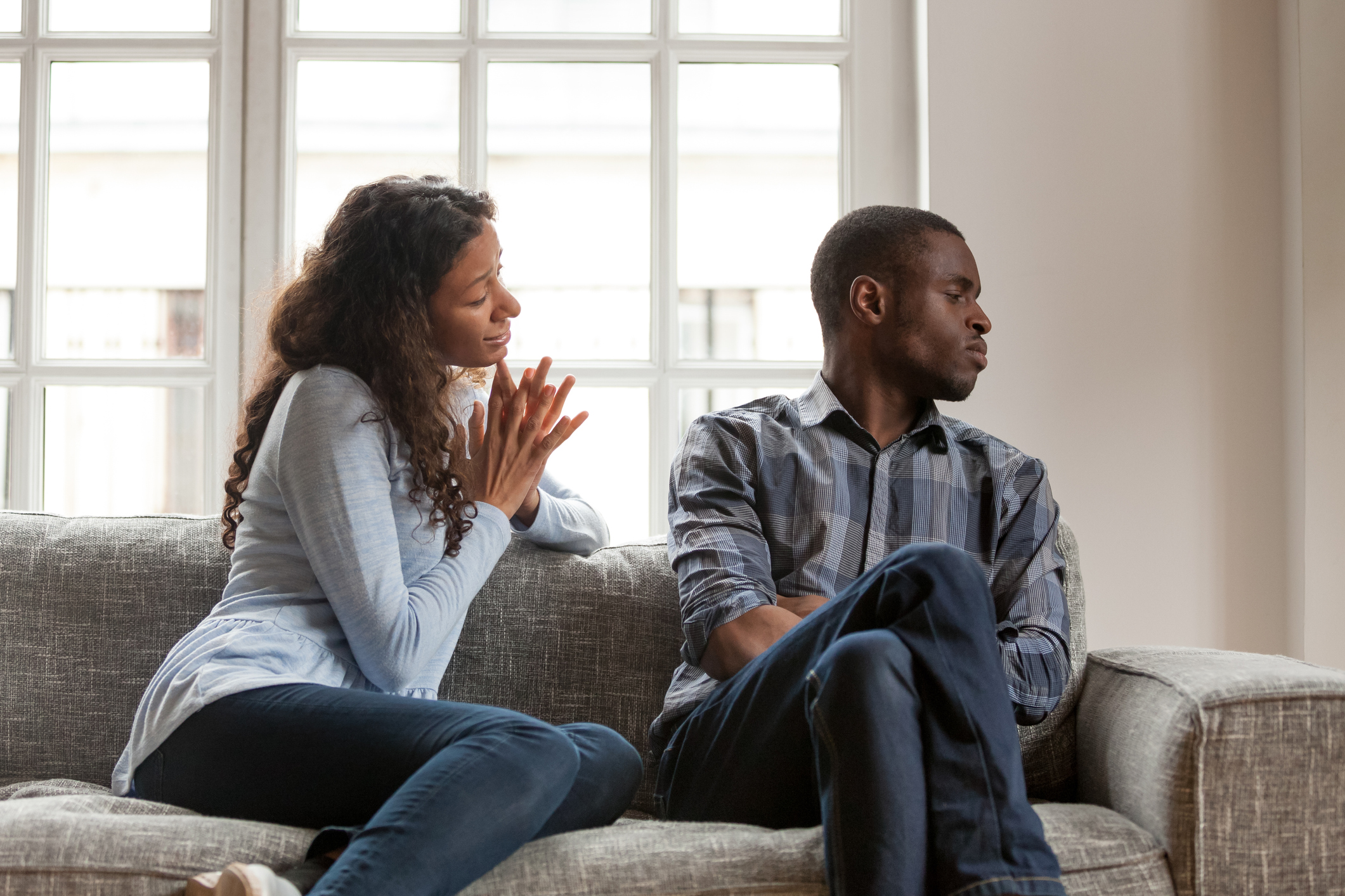 Angry husband and guilty wife sitting on couch at home