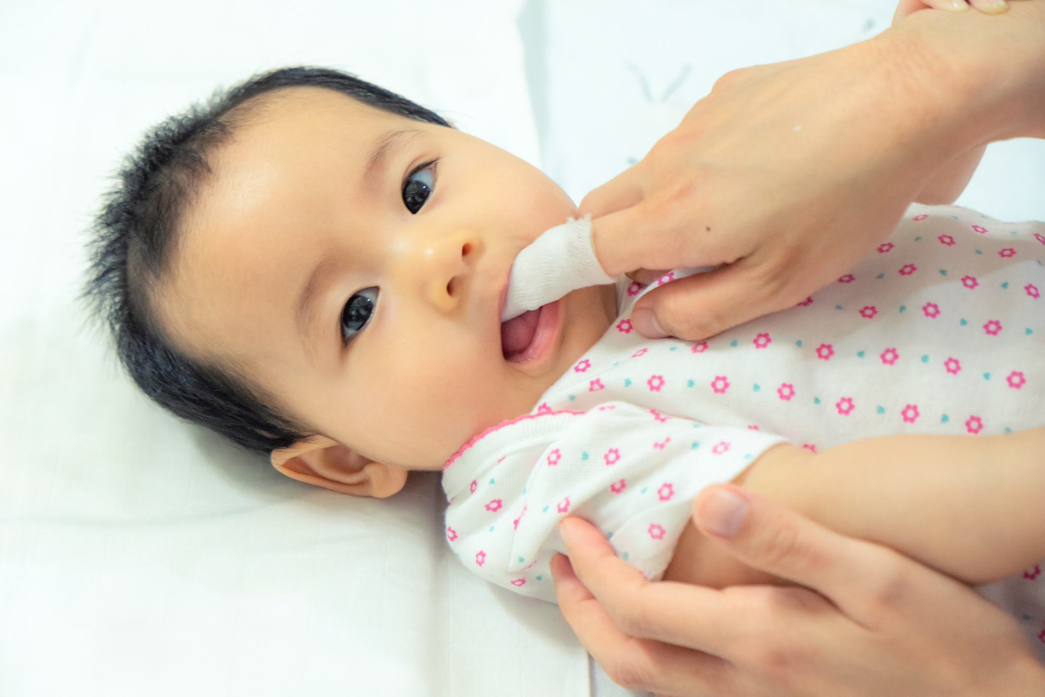 Mother use finger to clean asian baby tongue with clean gauze.