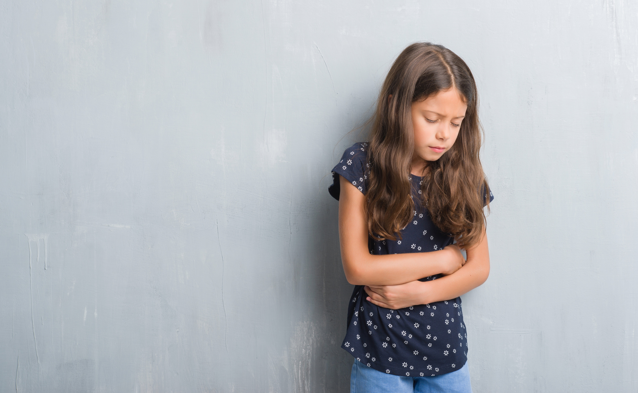 Young hispanic kid over grunge grey wall with hand on stomach because indigestion, painful illness feeling unwell. Ache concept.