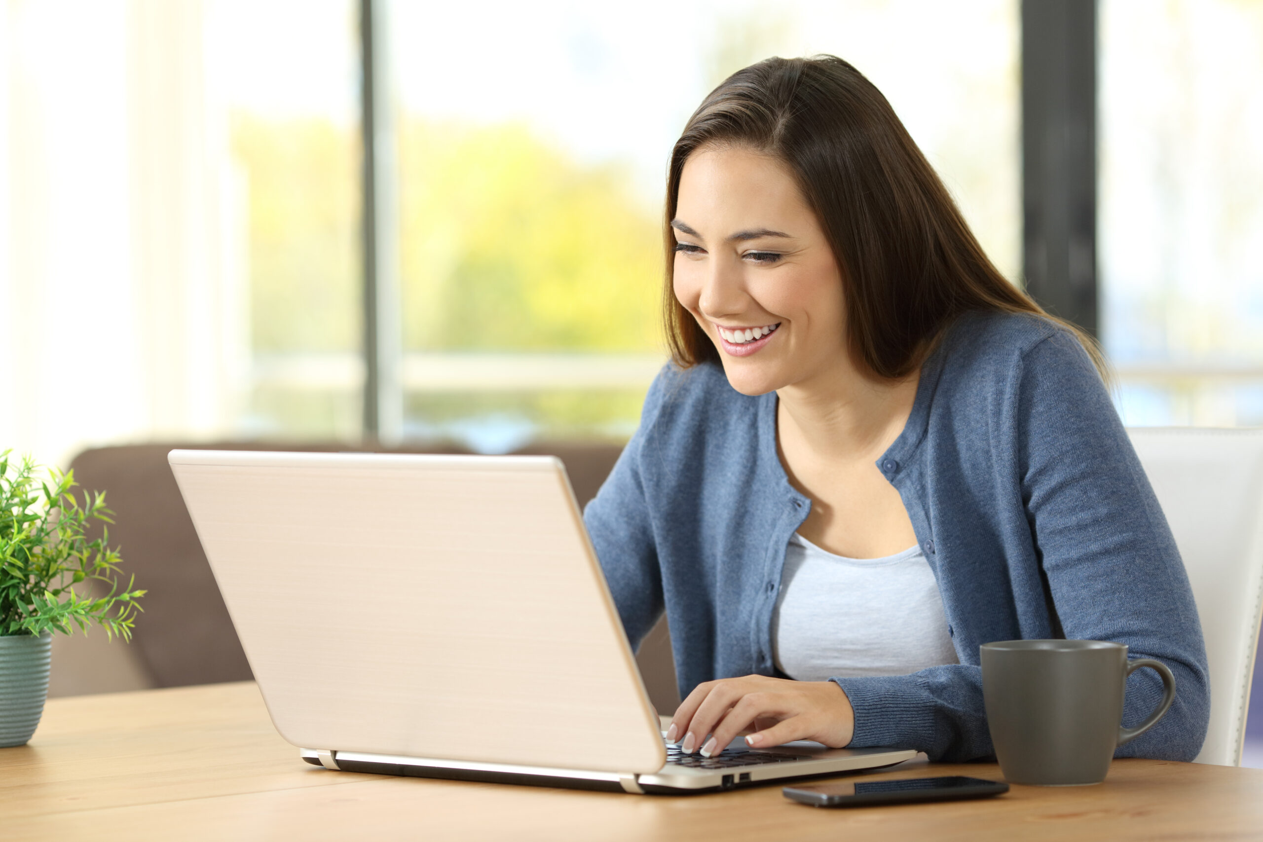 Woman writing in a laptop on a desk at home