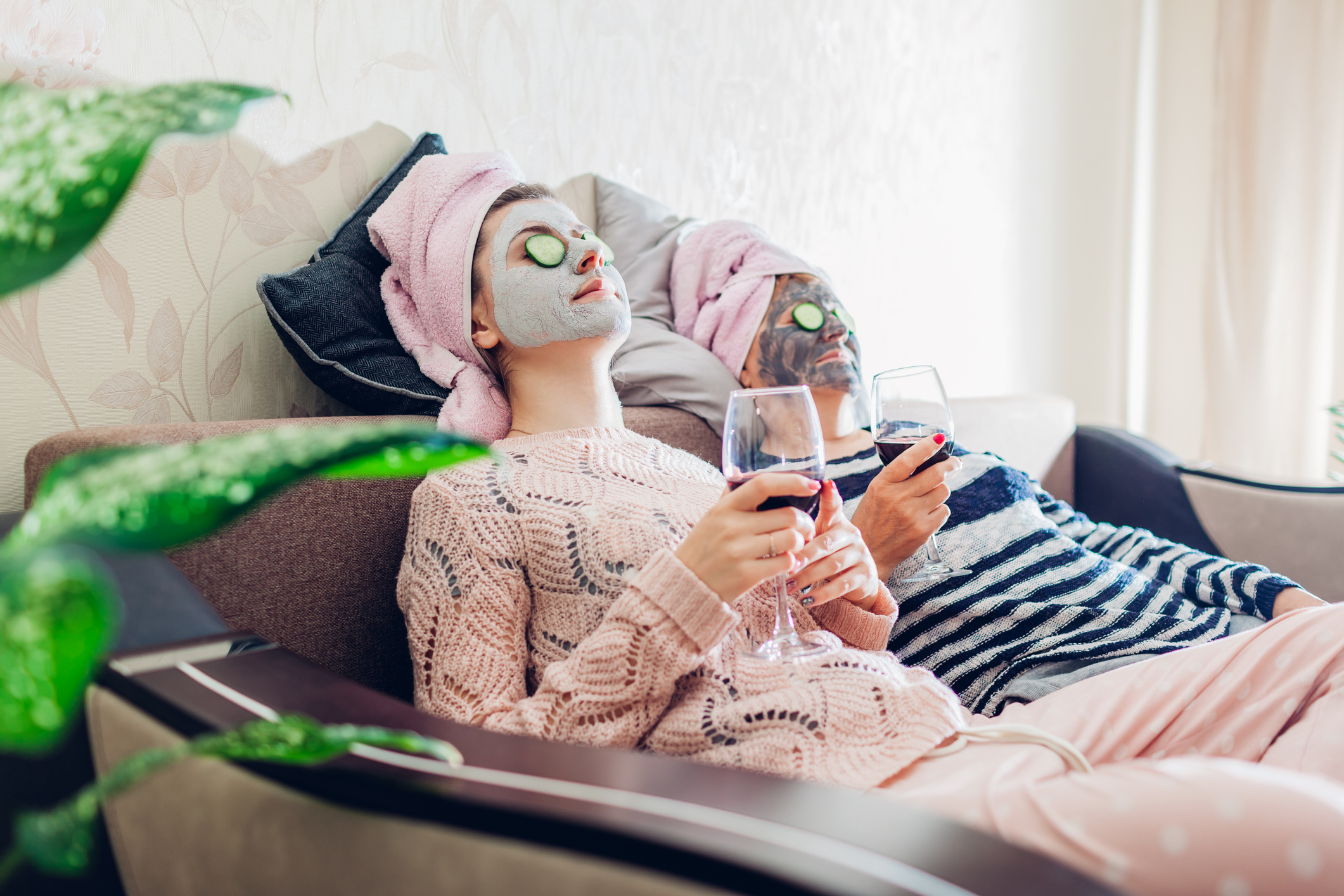 Mother and her adult daughter applied facial masks and cucumbers on eyes. Women chilling while having wine